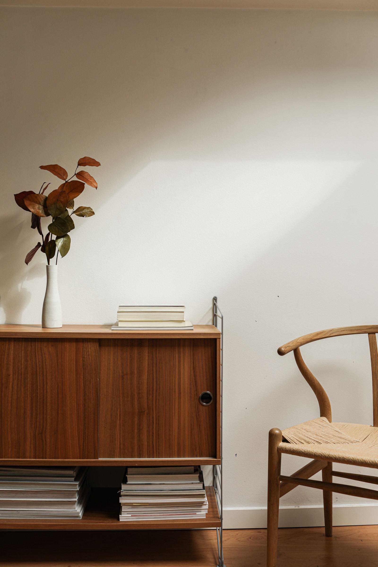 A calm room with a wooden sideboard, a small plant and a chair in soft light
