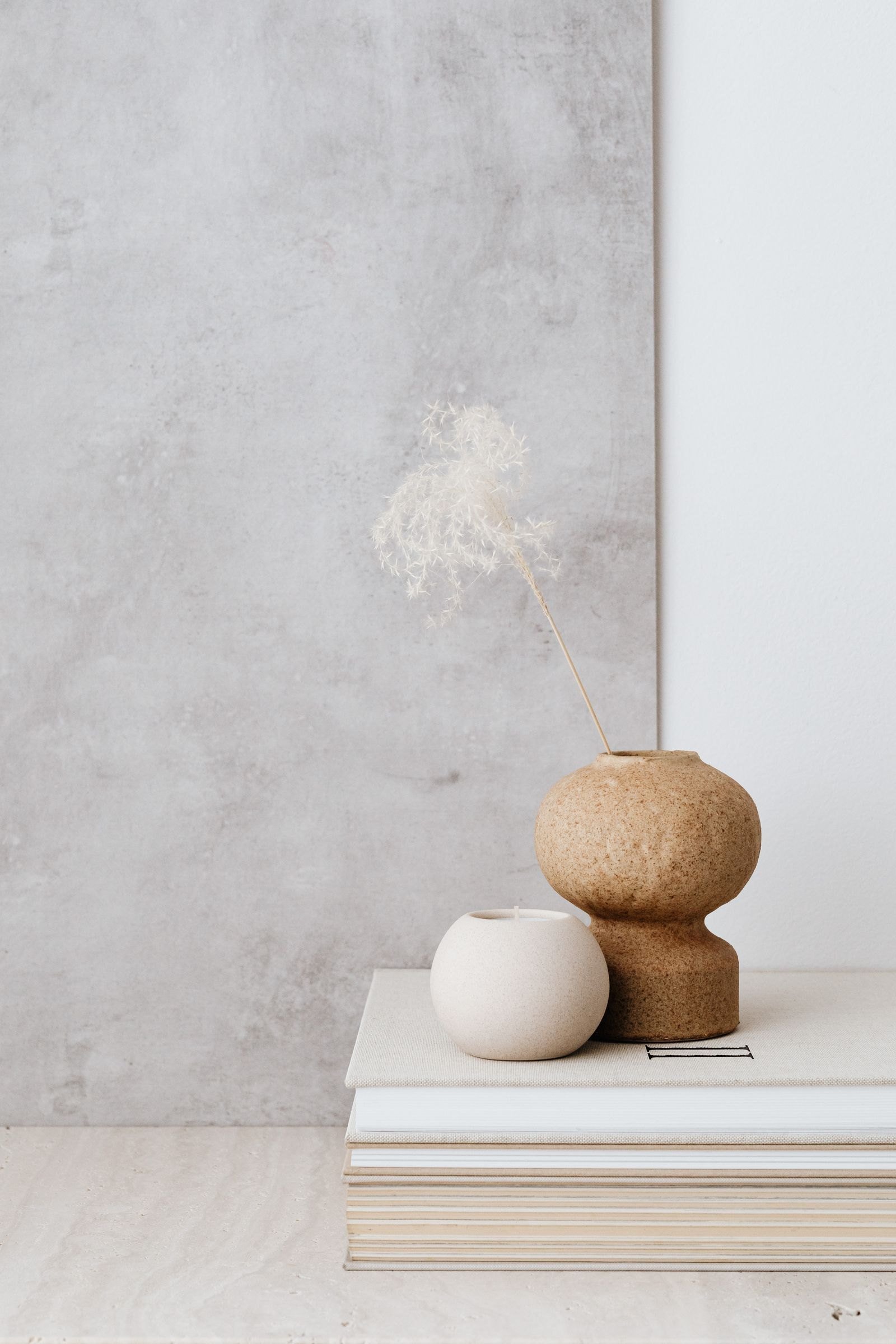Soft ceramic vases on a stack of books against a grey wall