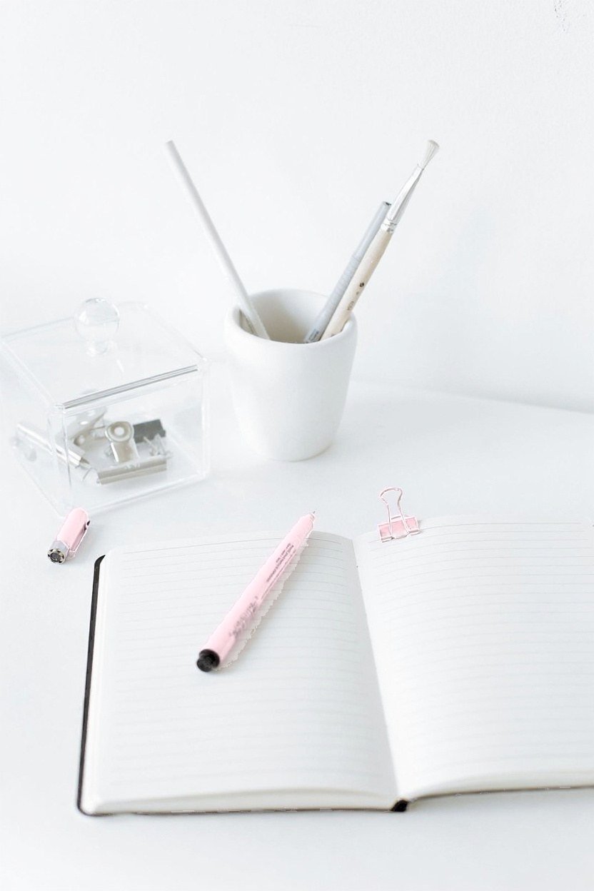 An open notebook with a pale pink pen on a clean white desk