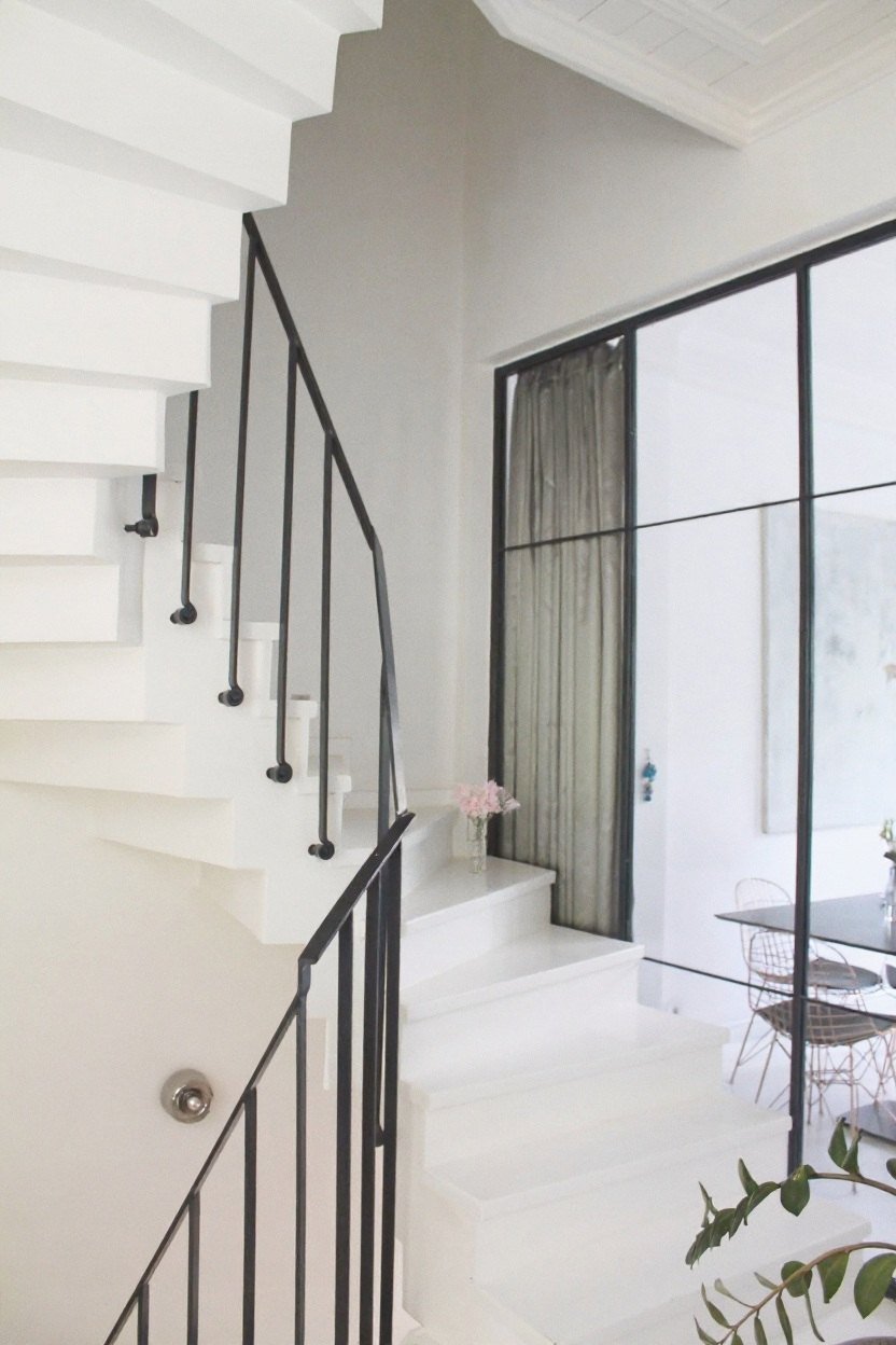 A bright white stairwell with a black railing and a small vase of pale pink flowers
